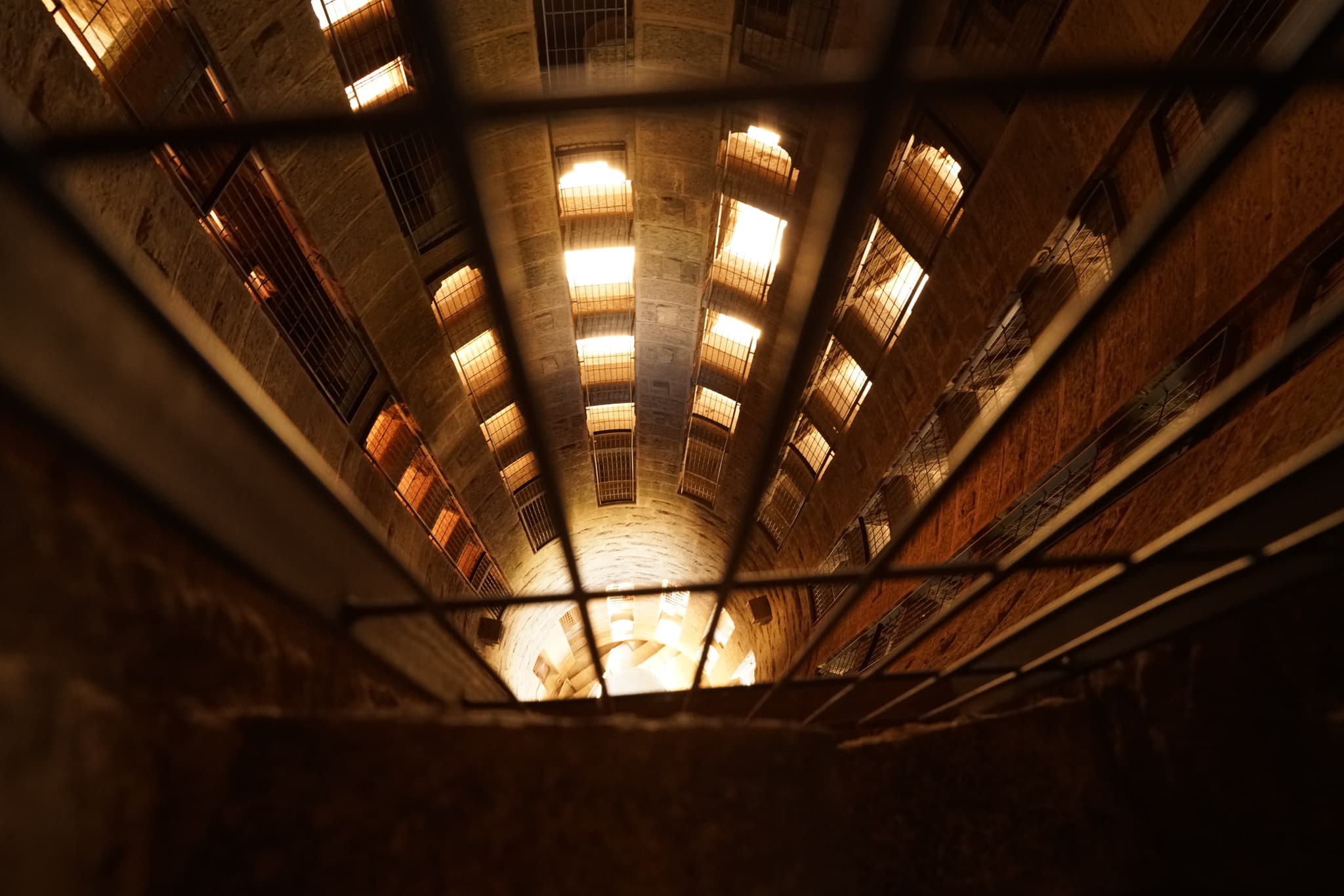 A view from the bottom of a deep, illuminated shaft or well-like structure with a grid or grate at the top, creating a perspective of depth and confinement