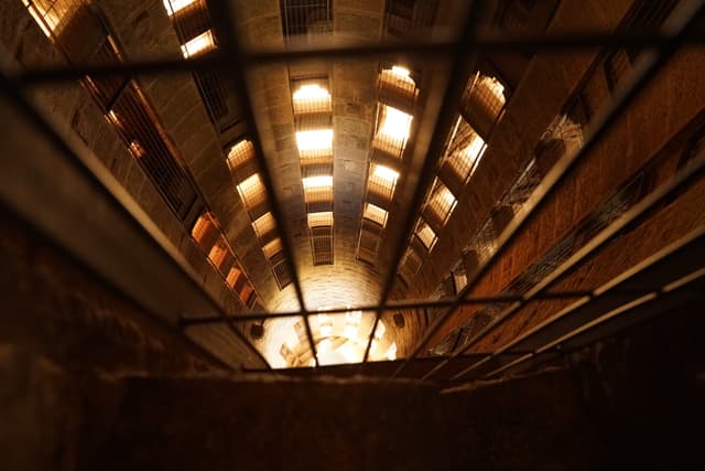 A view from the bottom of a deep, illuminated shaft or well-like structure with a grid or grate at the top, creating a perspective of depth and confinement