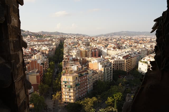A panoramic view of a densely built cityscape with numerous buildings stretching into the distance, framed by an opening that could be a window or a gap between structures